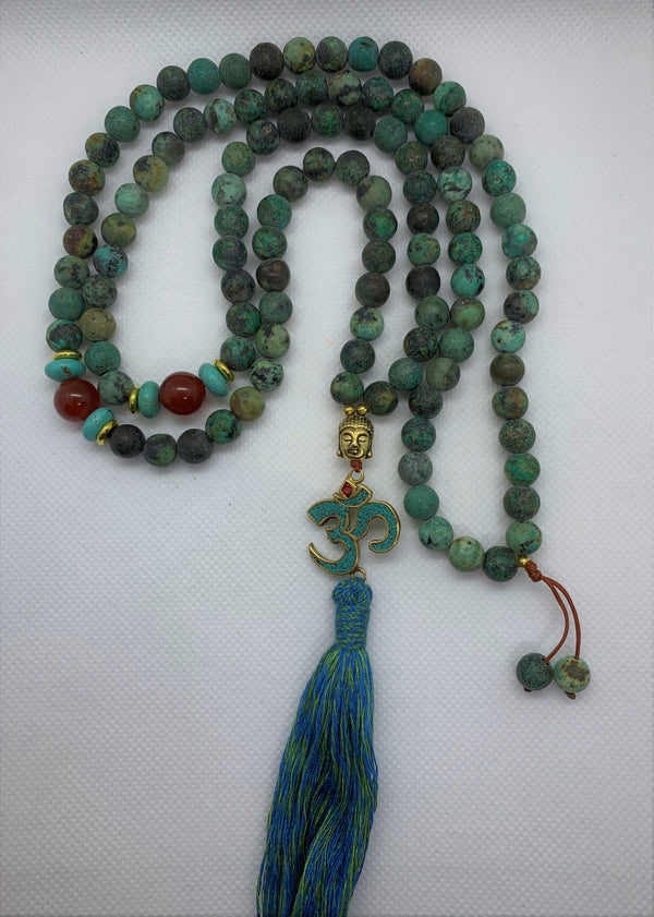 The Evolution Mala with African Turquoise and Carnelian beads necklace features a Buddha & Om symbol pendant, symbolizing the persistence and teachings of Buddha and the most fundamentally strong sound of the universe - Om.