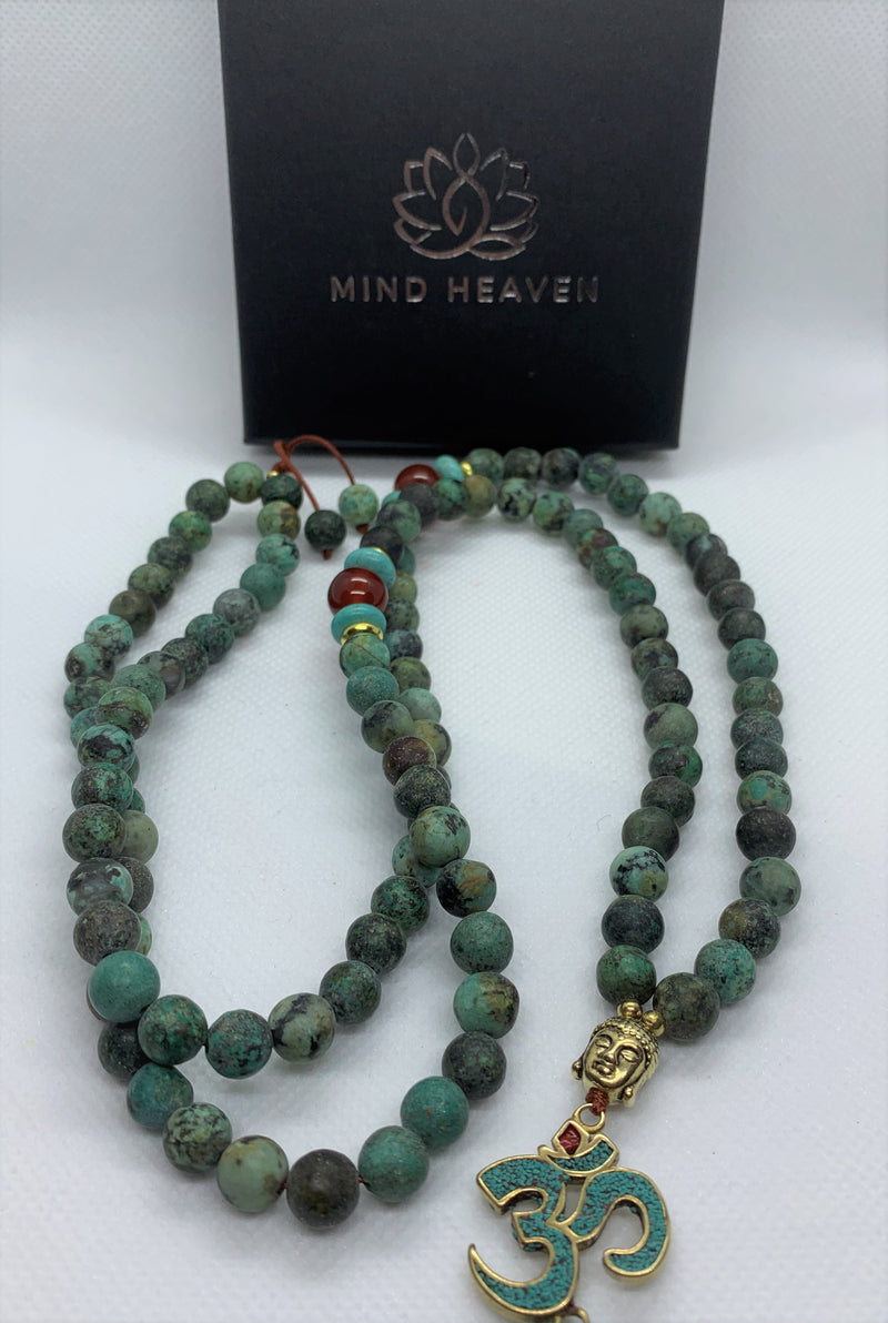 The Evolution Mala with African Turquoise and Carnelian beads necklace features a Buddha & Om symbol pendant, symbolizing the persistence and teachings of Buddha and the most fundamentally strong sound of the universe - Om.
